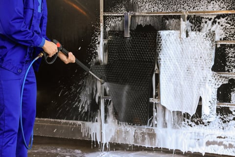Worker cleaning auto mats with high pressure water jet at car wash