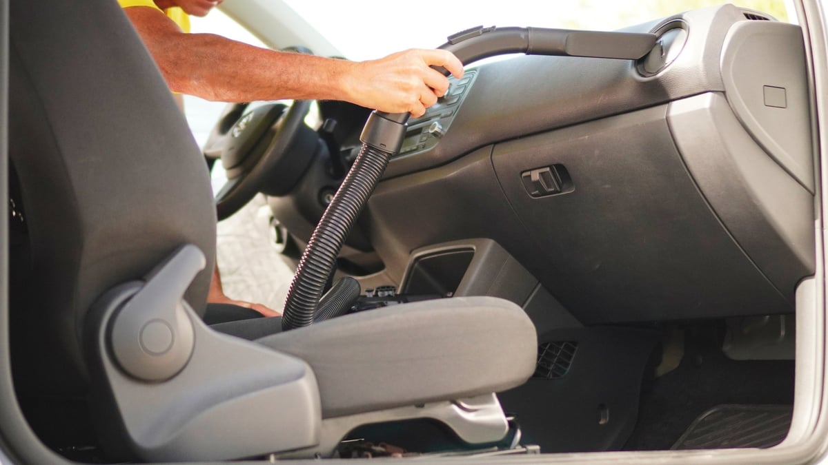 Close-up of an arm and hand using a vacuum cleaner to clean the interior of a car. The image highlights the precise action and use of the vacuum