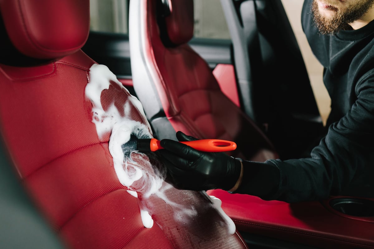 Professional detailer brushing car leather seat with cleaning solution during interior detailing procedure