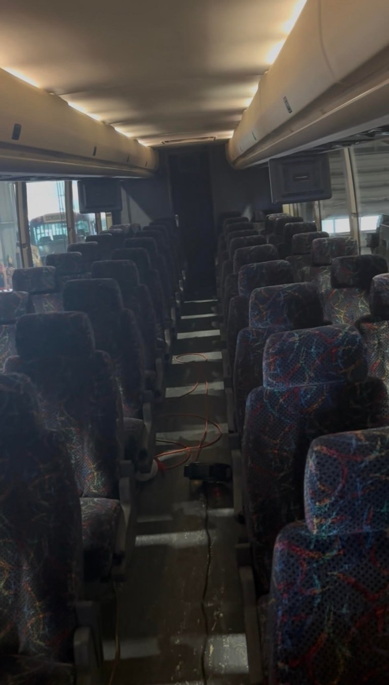 Interior of a coach or tour bus with rows of patterned seats, LED ceiling lights, and windows along both sides