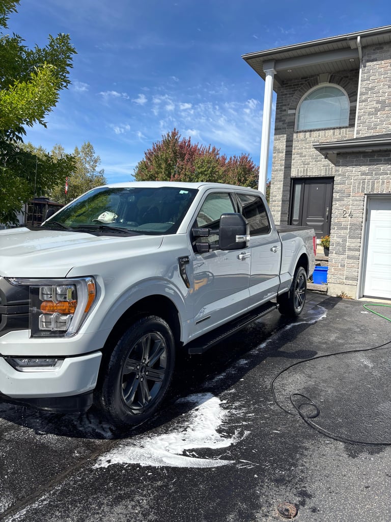 White Ford F-150 pickup truck parked in driveway of brick house on sunny day