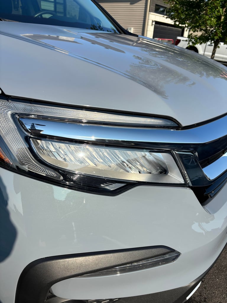 Close-up of a white cars front end showing the headlight, hood, and bumper in daylight