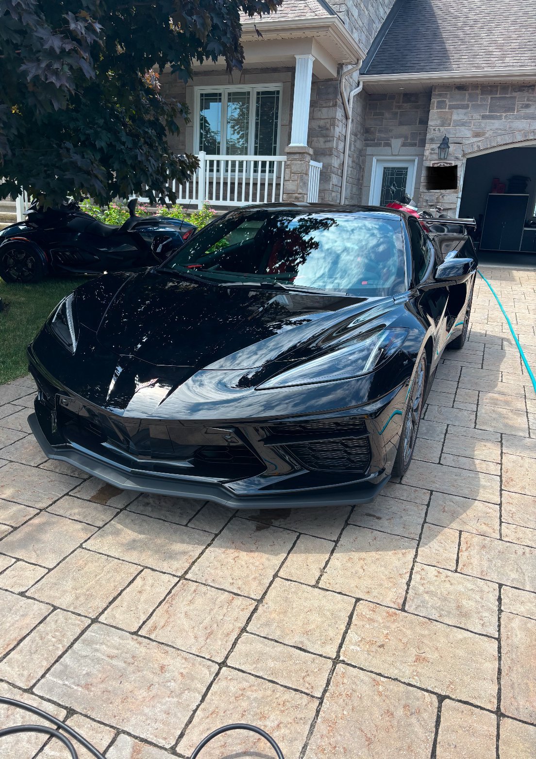Black sports car parked in driveway of stone house with white pillars and ivy-covered entrance